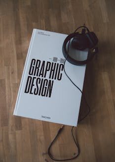 Discover graphic design history with this book and headphones on a wooden floor.